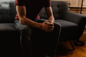 A man sitting on a couch with hands clasped requiring to find the right licensed therapists near him