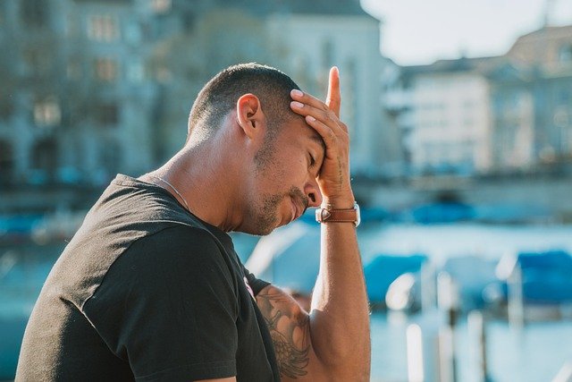 Distressed man placing his hand on forehead expressing need for individual therapy for men in denver