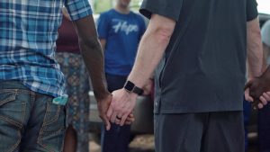 Men forming a circle and holding hands at a therapy session, showing support and solidarity