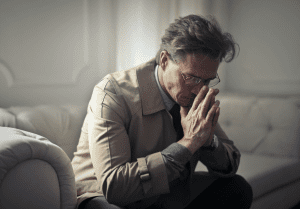 Man sitting upset on sofa at home and lost in troubled thoughts.