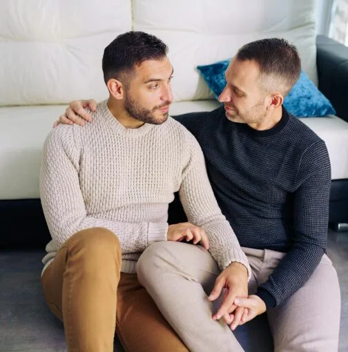 A gay couple sitting on the couch, hands intertwined, while discussing lgbt couples therapy in Denver