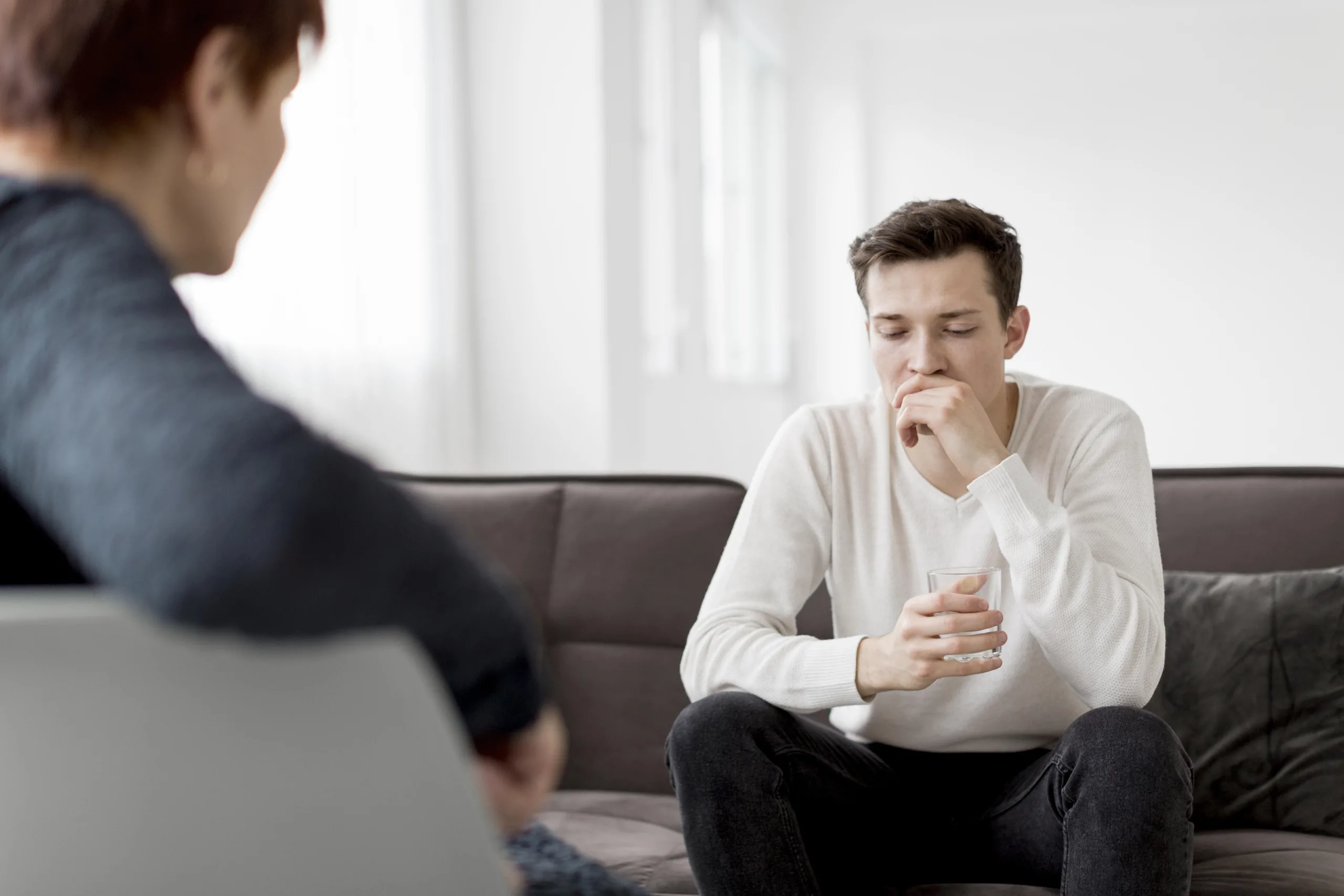 A man sits on a couch in a clinic, reflecting on his emotions, a moment that captures the essence of grief counseling.