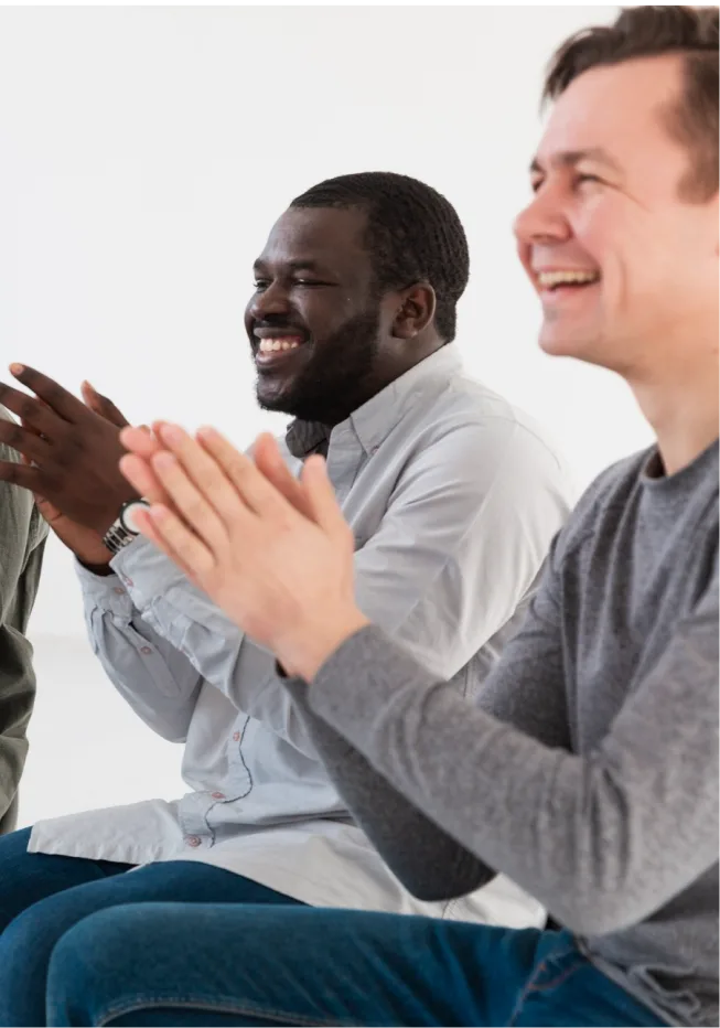 Men cheering and showing support for a fellow member in a men’s group therapy session.