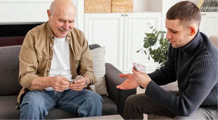 An elderly man joyfully playing cards with his son after healing from past traumas through EMDR therapy.