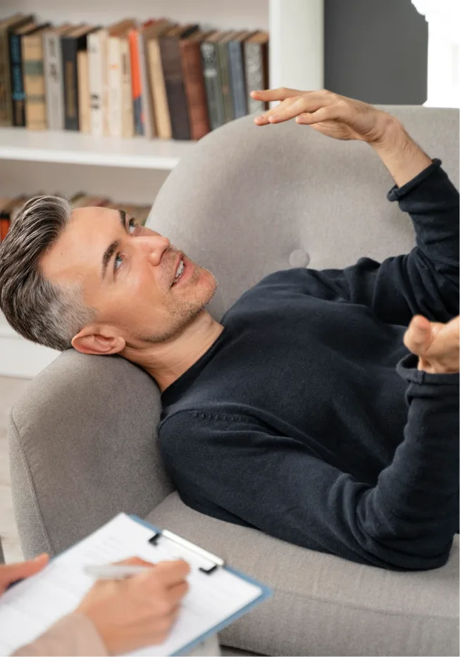 Man lying on a sofa, engaging in conversation with his therapist during a psychedelic-assisted therapy session.