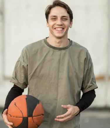 Young man holding a basketball, smiling confidently after teen counseling in Denver