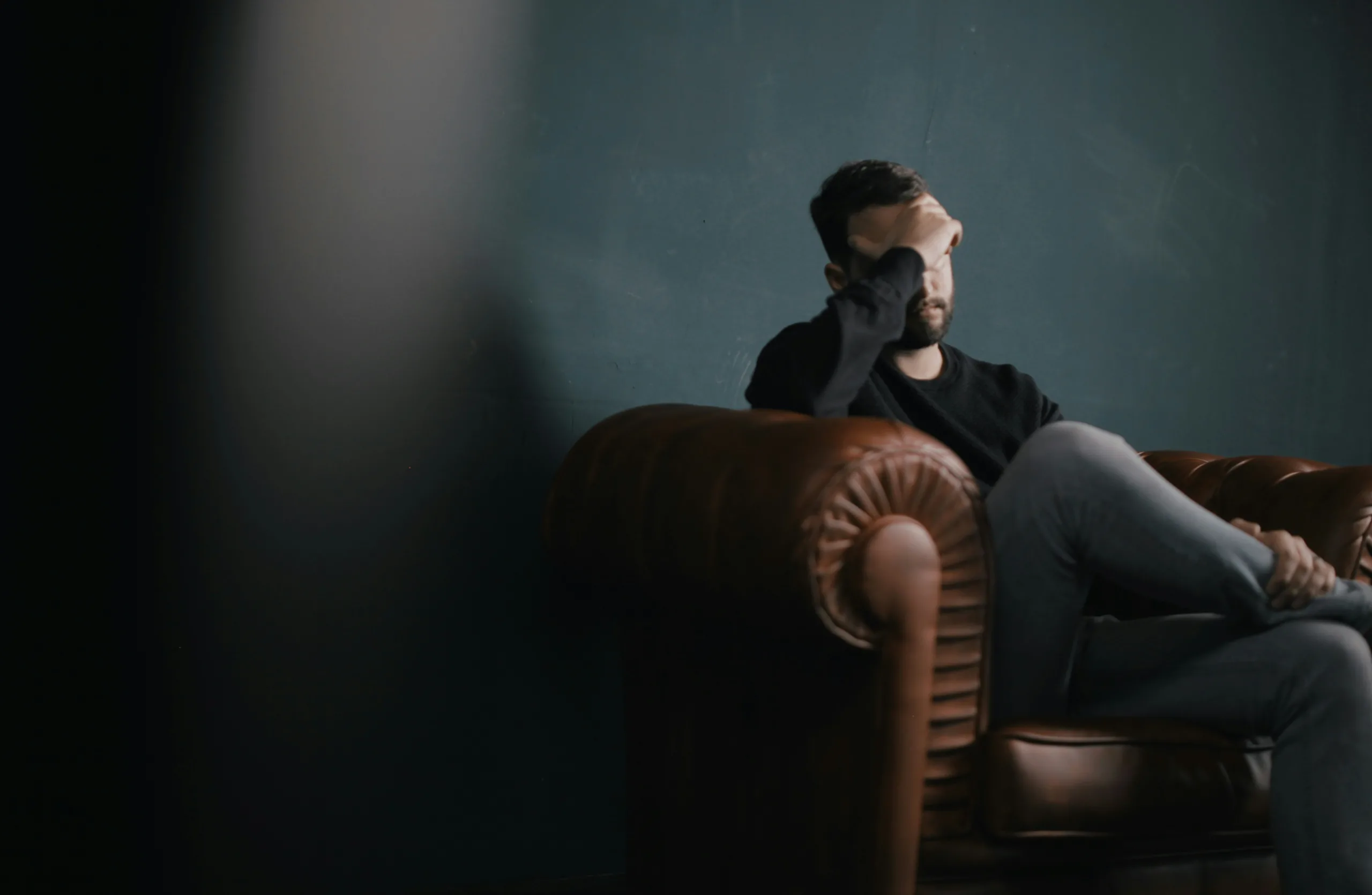 Man sitting on couch with hand on forehead, reflecting emotional impact of different types of PTSD disorders